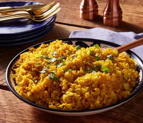Fotografía de un bol de arroz amarillo sazonado con cilantro, sobre mesa de madera