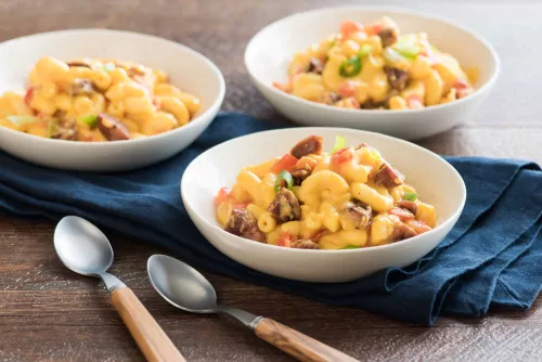 Fotografía de tres tazones con macarrones con queso, trozos de tocino y guisantes sobre mesa