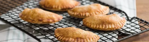 Fotografía de empanadas horneadas doradas en rejilla sobre paño a cuadros