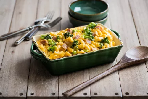 Fotografía: cazuela verde con macarrones gratinados, guisantes y trozos de jamón sobre tabla