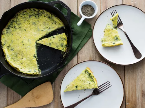 Fotografía de frittata con hierbas en sartén de hierro y dos porciones en platos blancos