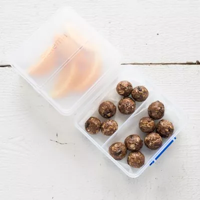 Fotografía: tupper transparente abierto con bolitas energéticas marrones sobre mesa blanca