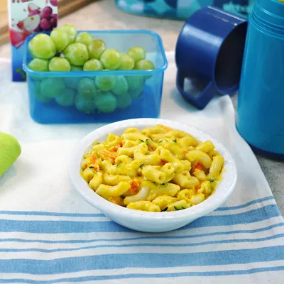 Fotografía de bol de pasta cremosa con verduras y contenedor de uvas verdes