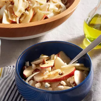 Fotografía de tazón azul con pasta en tiras, manzana y nueces; botella de aceite.