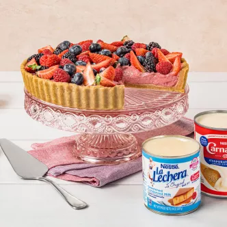 Strawberry and mixed-berry tart on pink glass stand with two milk cans and server
