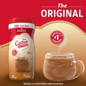 Una lata de creamer en polvo Coffee mate Original con una tapa roja y una etiqueta roja encima de una taza de café y un biscotti.