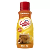 Una botella de creamer Hazelnut con una etiqueta roja encima de una taza de café, avellanas enteras y el logotipo del producto.