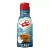 Una botella azul de creamer Coffee mate Coconut Crème con una tapa roja y una etiqueta azul sobre una taza de café y un coco.