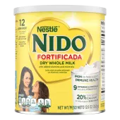 Una lata de Nido Fortificada con una etiqueta amarilla, una tapa blanca y un corazón dorado sobre un vaso de leche vertida.