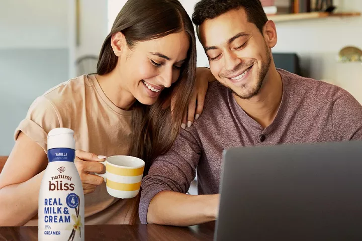 Hombre y mujer sentados frente a una computadora portátil en un escritorio con frasco de creamer natural bliss de vainilla.