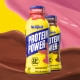 Waves of strawberry and chocolate milk behind bottles of strawberry and chocolate Protein Power.