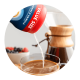 Powder pours from a canister into a mug of coffee near a pour over coffee maker.